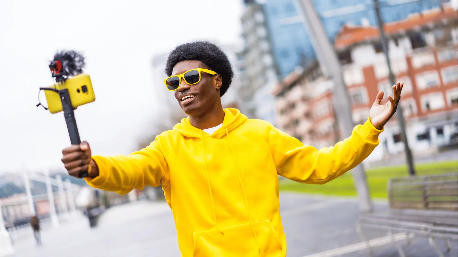 Young man in yellow hoodie vlogging outdoors with phone on handheld gimbal for AI-assisted workflow