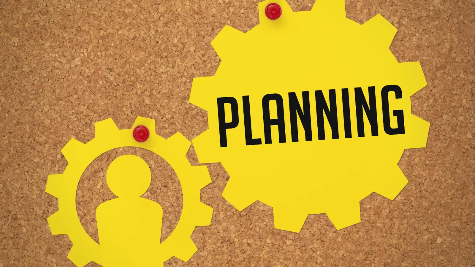 Yellow paper gears pinned to corkboard, one reads 'PLANNING' with person silhouette