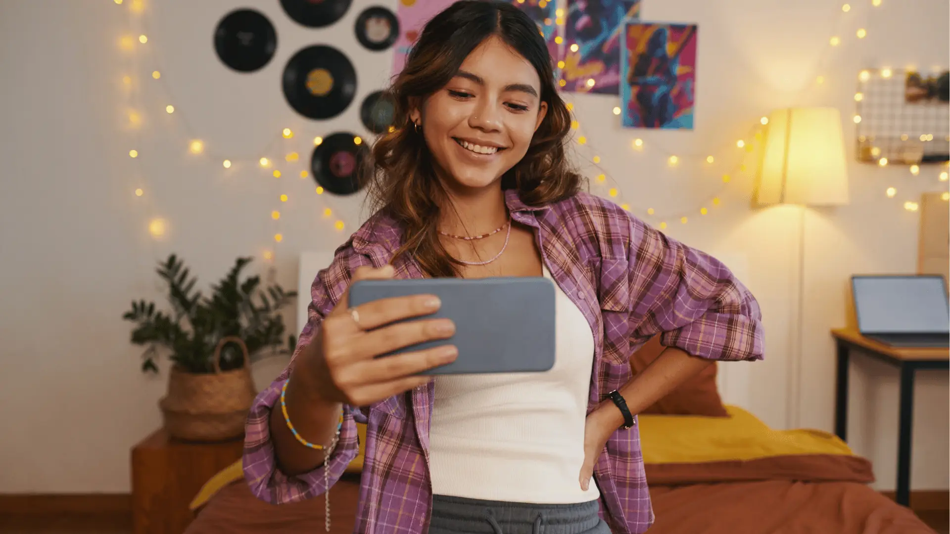 Young woman smiling while holding a smartphone in decorated bedroom